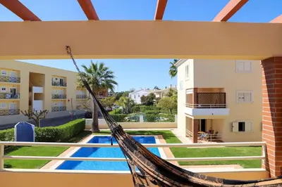 a hammock hanging from a building with a pool at Atlântida Golf Village by Garvetur in Quarteira