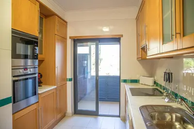 a kitchen with wooden cabinets and a sliding glass door at Terraços do Milénio II by Garvetur in Quarteira