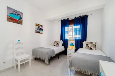a bedroom with two beds and a window with blue curtains at Sol & Mar Quarteira in Quarteira