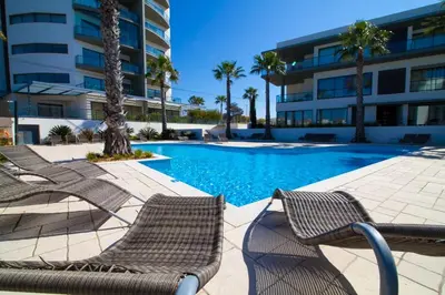 a pool with chairs and palm trees and a building at Cavalo Preto Beach Resort Apt & Wi-Fi Nr Beach in Quarteira