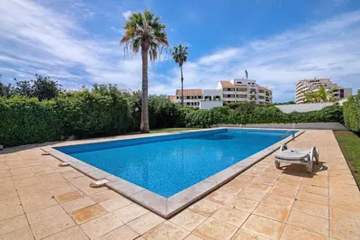 a blue swimming pool with palm trees and a building at Apartamento Machadinho in Albufeira