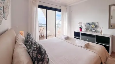 a white bedroom with a large bed and a window at Ocean View Quarteira in Quarteira