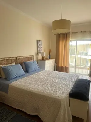 a bedroom with a bed with blue pillows and a window at Jardins da Marina BQ in Albufeira