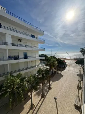 a building with palm trees in front of the beach at Beach House in Quarteira