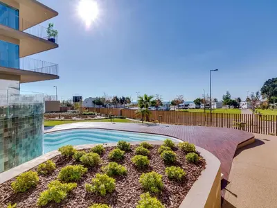a swimming pool with plants in front of a building at 2bdr Horizon Sand apartment in Quarteira in Quarteira