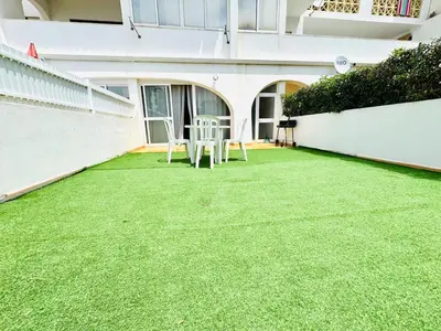 a patio with two chairs and a table on the grass at Apartamento gourmet com quintal in Albufeira