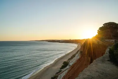 a beach with the sun setting over the ocean at Pine Cliff Apartment by The Portuguese Butler in Olhos de Água