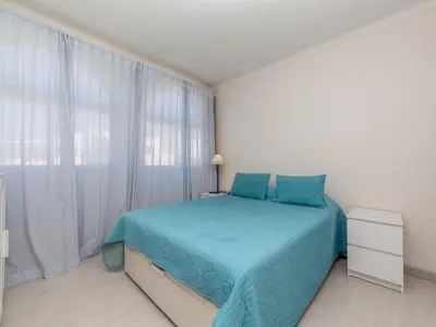 a white bedroom with a blue bed and a window at Akisol Albufeira Eris in Albufeira