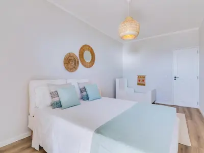 a white bedroom with a large white bed with blue pillows at Apartamento Vida Pura com 2 quartos e vista mar in Quarteira