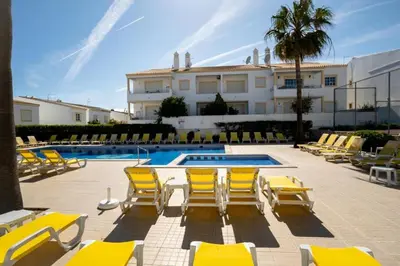 a swimming pool with yellow chairs and a building at Casa Sol Dourado in Albufeira