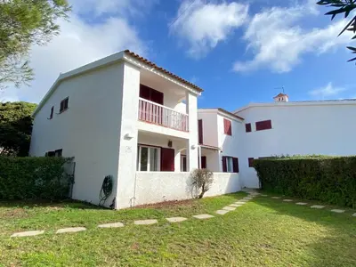 a white house with red windows and a green yard at Casa Manacá Vilamoura in Quarteira