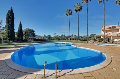 a large blue swimming pool with palm trees in the background at Las Palmeiras Vilamoura in Quarteira