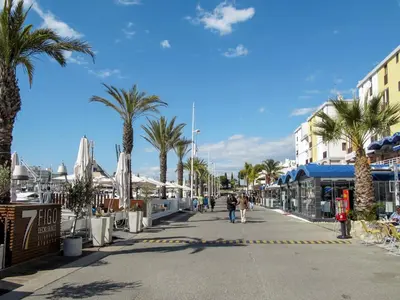 people walking down a street with palm trees and buildings at Holiday Home Aldeia Do Mar by Interhome in Vilamoura