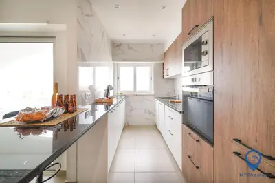 a kitchen with white counters and a large window at Palmeiras by MTPhomes in Albufeira