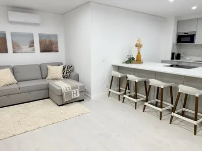a kitchen and living room with a gray couch and stool at Sunrise Apartment in Albufeira