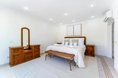 a white bedroom with a bed and a wooden dresser at Villa Mia - Vale do Lobo in Vale do Lobo