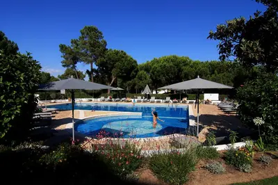 a woman is swimming in a swimming pool with umbrellas at Apartamentos Valverde - Quinta do Lago in Quinta do Lago