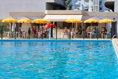 a swimming pool with people sitting under umbrellas at Cheerfulway Minichoro Apartamentos in Albufeira
