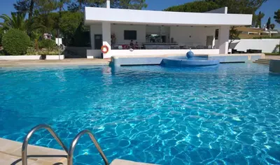 a swimming pool with blue water in front of a house at Blue&Greens Apartment in Quinta do Lago