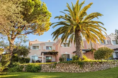 a pink house with palm trees and a stone wall at Vilar do Golf in Quinta do Lago