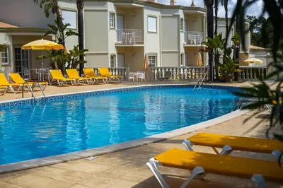 a swimming pool at a hotel with yellow chairs and a building at Vila do Castelo in Albufeira