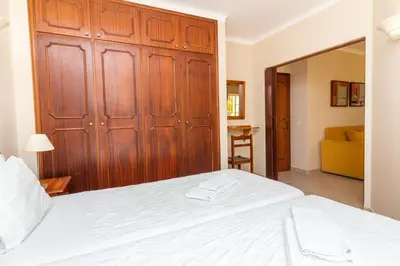 a bedroom with a white bed with a wooden closet at Vila do Castelo in Albufeira