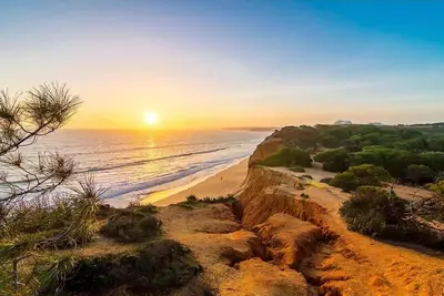 a view of a beach with the sun setting at Olhos de Água Apartment Albufeira in Albufeira