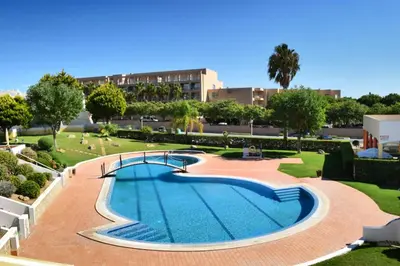 a swimming pool in a park with trees and buildings at Townhouse 700m from Sao Rafael Beach in Albufeira
