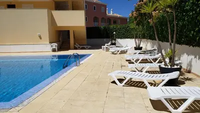 a pool with white lounge chairs next to a building at Marina Vilamoura Apartment in Vilamoura