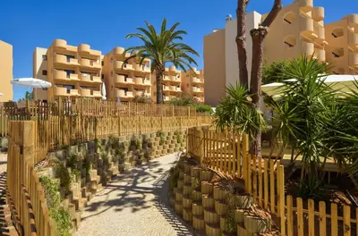 a fence with palm trees and buildings in the background at 3HB Falésia Garden in Albufeira