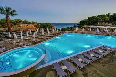 a swimming pool with chairs and the ocean at 3HB Falésia Garden in Albufeira