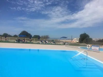 a blue swimming pool with people sitting on benches at Beachfront flat, private parking, pools, sea at less than 200 m in Albufeira