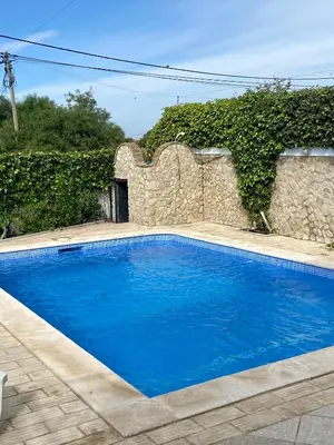 a blue swimming pool in front of a stone wall at Vivenda Silvestre Family House in Albufeira