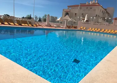 a large swimming pool with chairs and blue water at Albufeira Jardim 2 Studio in Albufeira