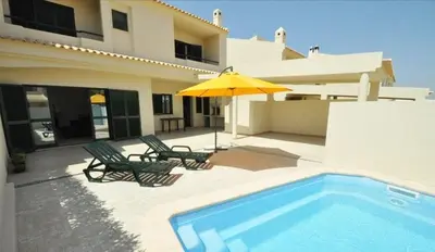 a house with a swimming pool and two chairs and an umbrella at Holiday House in Albufeira