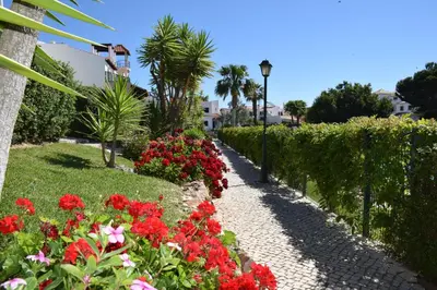 a garden with red flowers and a pathway at T4 Grand Townhouse Old Village in Vilamoura