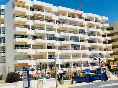 a large white building with flags in front of it at ACR Holiday Apartment in Quarteira