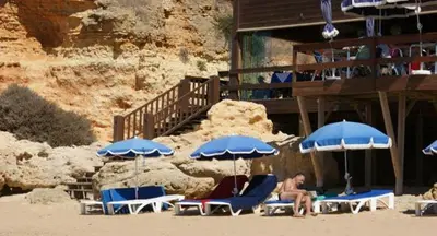 a man sitting on a beach with chairs and umbrellas at Villa V4 com Piscina Privada a 400 metros da Praia in Albufeira