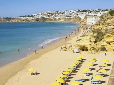a beach with yellow and blue umbrellas and people at Spacious house with private pool in Albufeira in Albufeira
