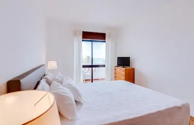 a white bedroom with a bed and a window at AL - Apartamento Girassol in Quarteira