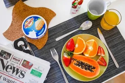 a plate of fruit on a table with a newspaper at The Albufeira Concierge - Modern Salgados in Albufeira