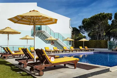 a swimming pool with lounge chairs and umbrellas at The Magnolia Hotel in Quinta do Lago