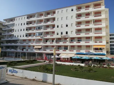a large white building with tables and umbrellas in front of it at Regueiró Quarteira Beach Apartment in Quarteira