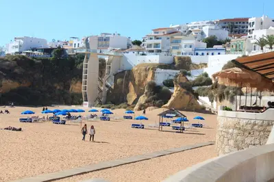 a beach with blue umbrellas and people on it at Apartamentos Colina do Mar Downtown Albufeira in Albufeira