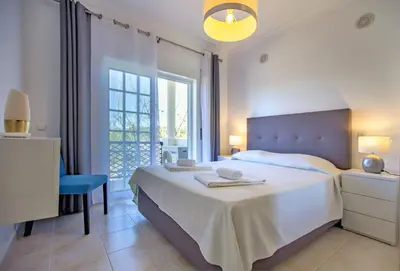 a white bedroom with a bed and a chair and a window at Olhos de Água Apartment Albufeira II in Albufeira