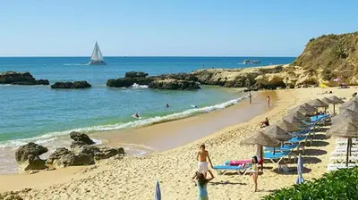 a beach with umbrellas and people swimming in the ocean at Praia dos Aveiros T1 - Albufeira INN in Albufeira