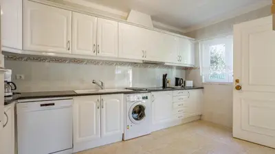 a kitchen with white cabinets and a washing machine at Villa Girassol in Vilamoura