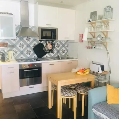 a kitchen with white cabinets and a table and a couch at Estúdio tranquilo praia da Falésia in Albufeira