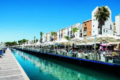 a canal with tables and umbrellas next to a city at Marina Vilamoura - Aquamar 401- Modern Apartment in Vilamoura