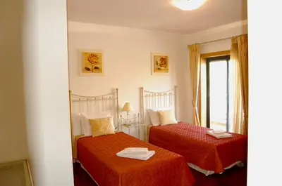 a bedroom with two beds with red sheets and a window at Corcovada in Albufeira